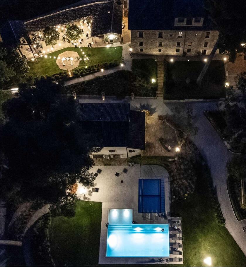 Veduta notturna di una villa con piscina illuminata e giardino per eventi.